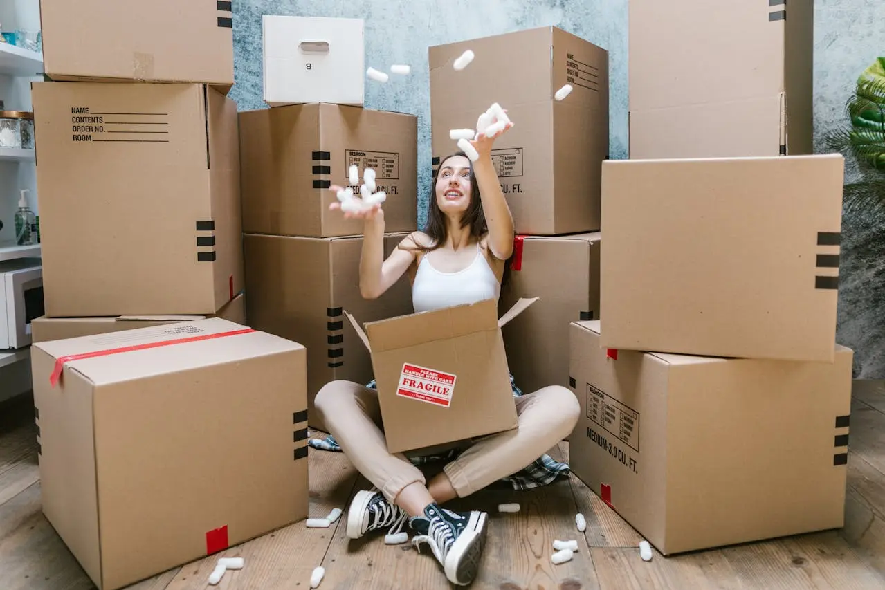 A woman sitting among cardboard moving boxes and packing materials