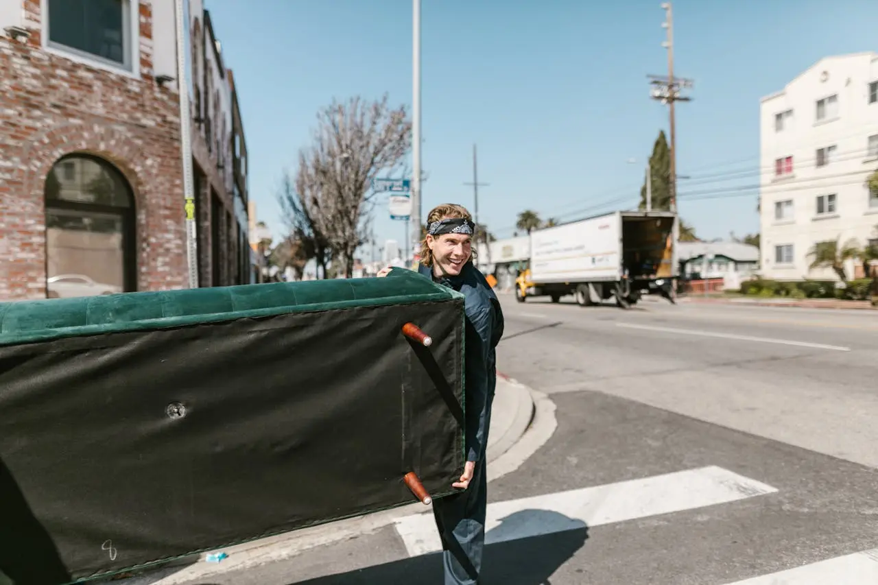 A person carrying a sofa outdoors, with a truck in the background