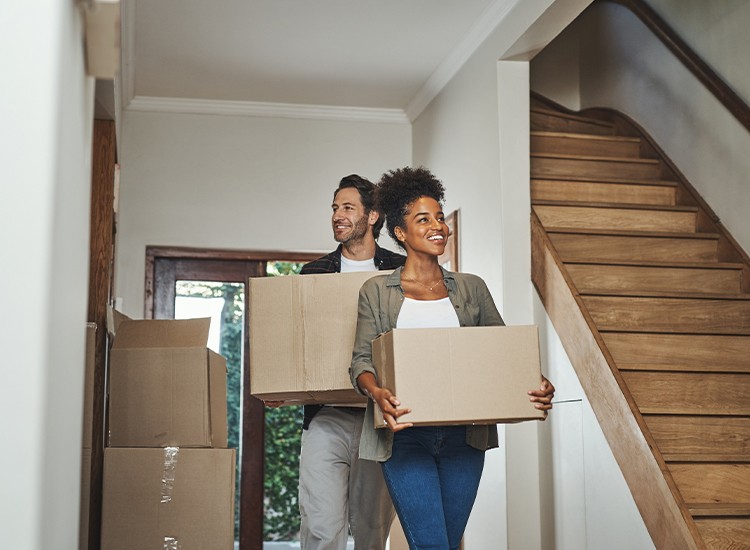 A couple carrying moving boxes into a home