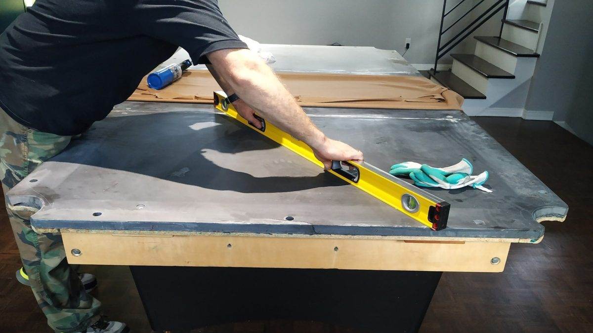 A person checking a pool table's exposed playing surface with a spirit level