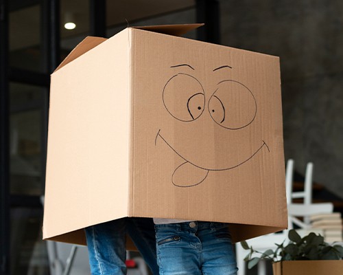 A person holding a cardboard moving box with a smiling face drawn on it